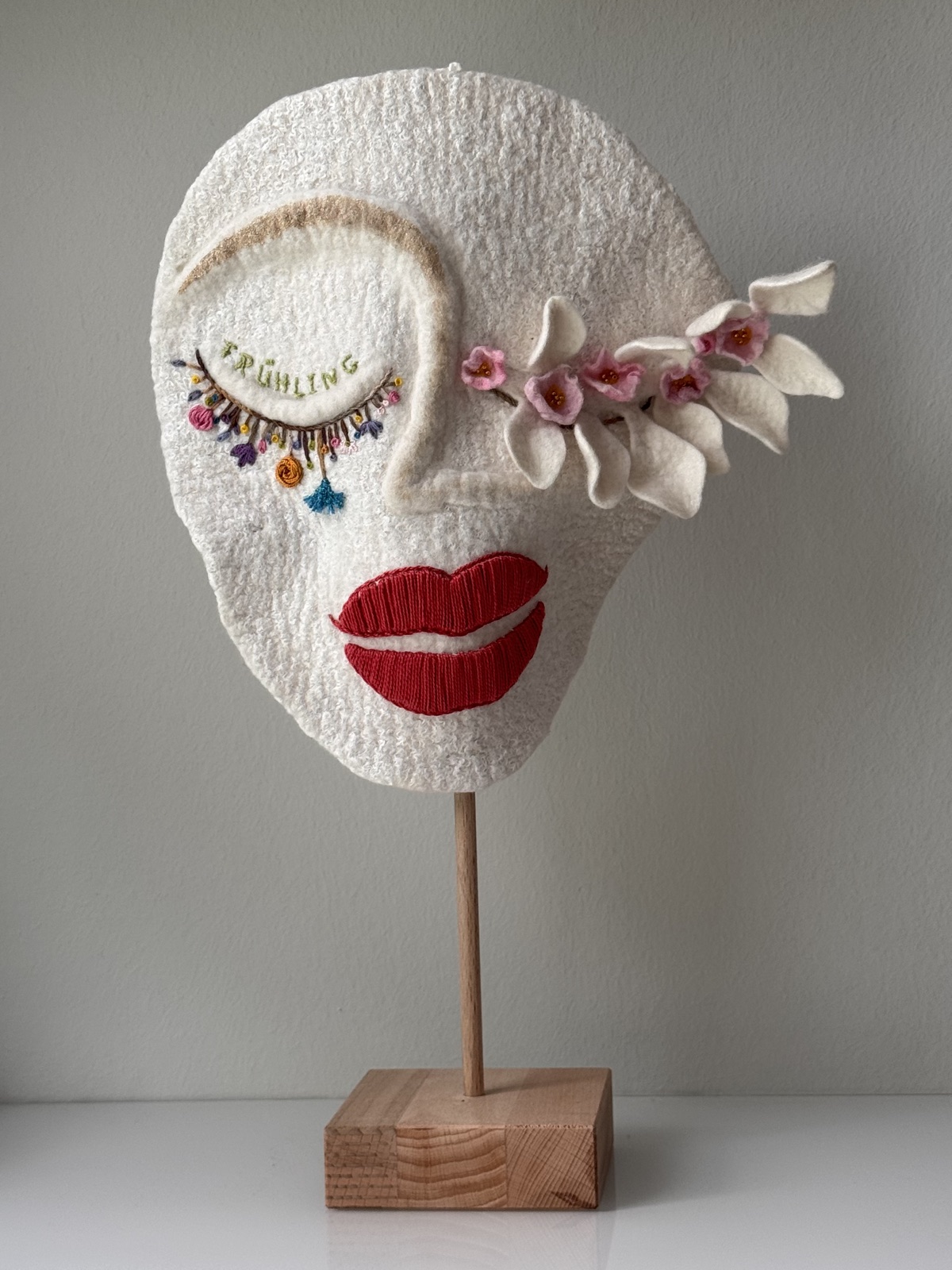 Handgefilzte weiße Maske „Schlafender Frühling“ mit gesticktem Wort Frühling auf dem Lid, Blütenzweig in Rosé und rotem Mund
